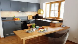 Eine moderne Küche mit grauen Schränken, einem Holztisch und einem Fenster mit Tageslicht.