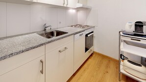 A modern kitchen with white cabinets, a granite countertop, stainless steel appliances, and a wooden floor. - Apartment building with excellent infrastructure. (St. Moritz)
