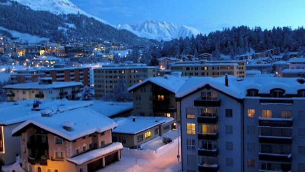 A snow-covered town with buildings and mountains in the background. - Apartment building with excellent infrastructure. (St. Moritz)