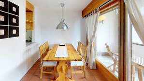 Un comedor con una mesa y sillas de madera, una lámpara colgante y vistas a través de una ventana con cortinas.