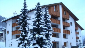 Un edificio de varios pisos con balcones y un árbol cubierto de nieve al frente.