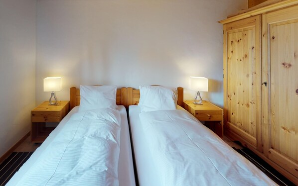 A double room with two beds, each with a bedside table and lamp, and a wooden wardrobe. - Very well located apartment house in the favorite and quiet Salet area. (St. Moritz)