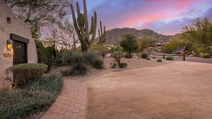 A desert landscape with a paved driveway leading to a building with a number '13251' on the wall.