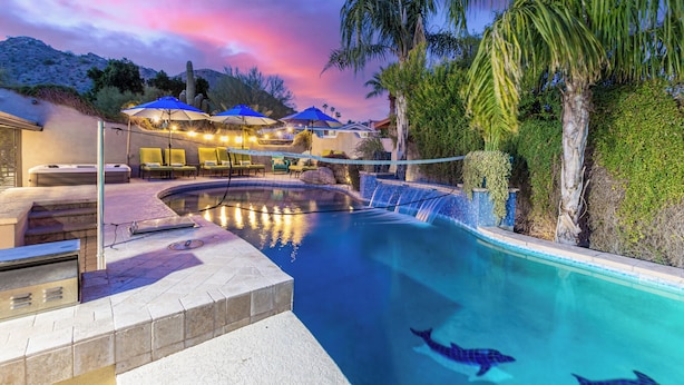 A swimming pool with a waterfall feature, lounge chairs, and umbrellas.