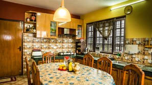 Une cuisine avec des meubles de rangement en bois, une table à manger recouverte d’une nappe à motifs floraux et divers appareils de cuisine.