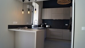 Une cuisine moderne dotée d’un îlot central, de luminaires suspendus et d’un revêtement mural noir.