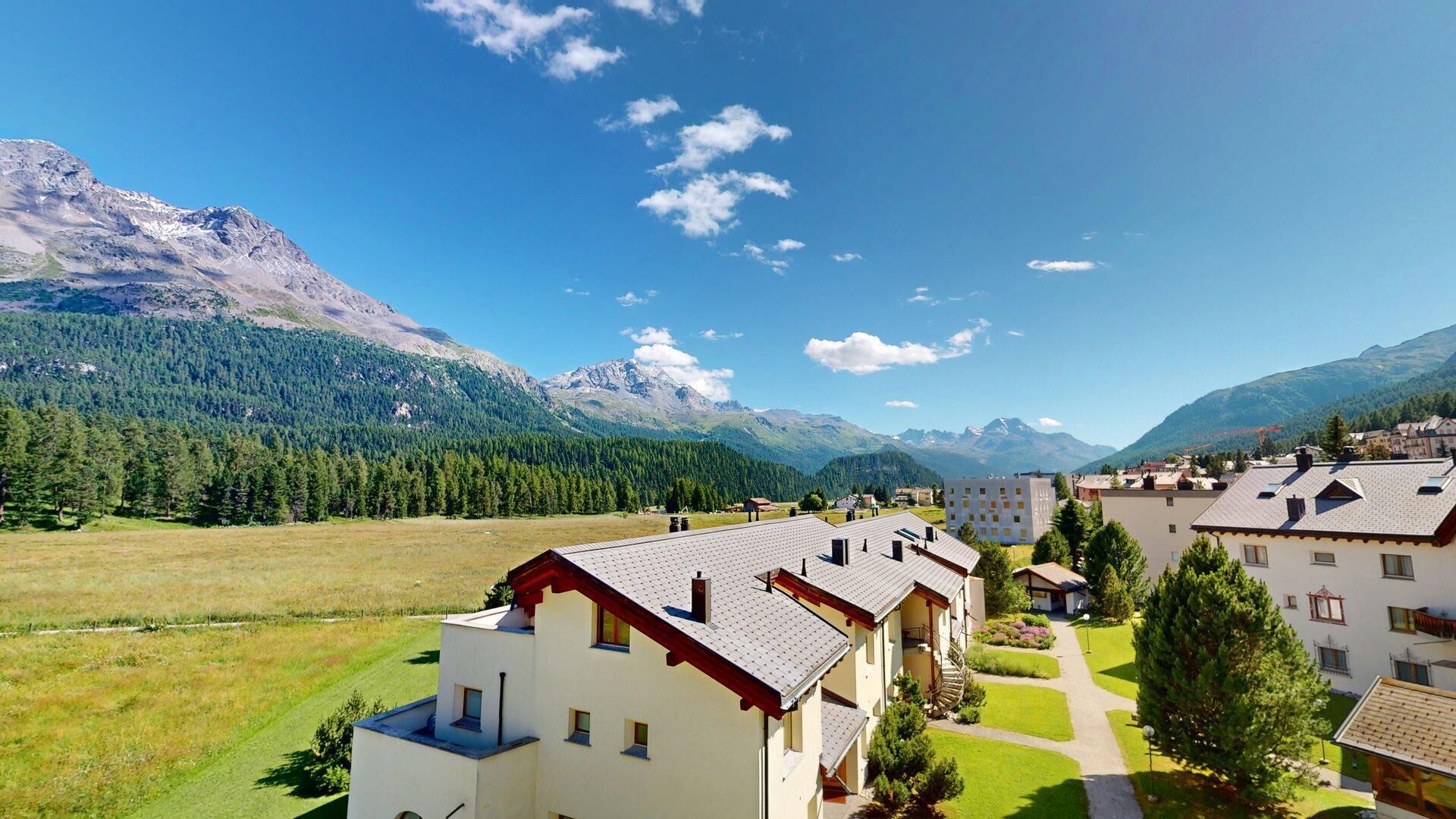 A modern building with a sloped roof, surrounded by a well-maintained lawn and a mountain backdrop.