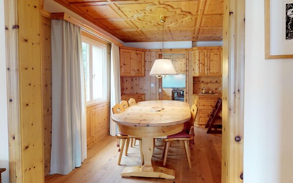 A wooden interior with a round dining table, chairs, a hanging lamp, and a kitchen area with wooden cabinets. - Relaxation in a luxurious duplex apartment (Champfèr)