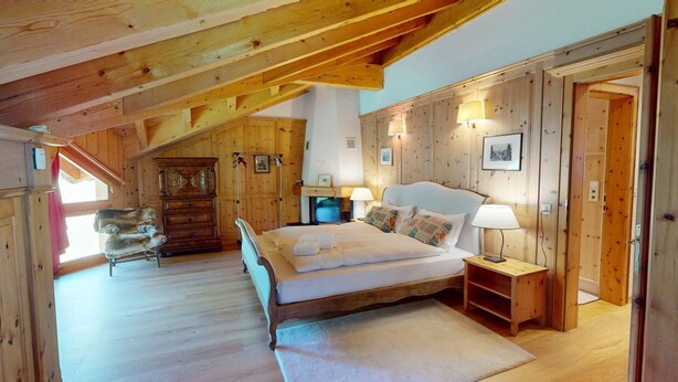 Une chambre confortable avec un plafond en bois, un grand lit, une chaise et une commode.