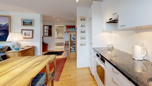 A modern kitchen with white cabinets, a granite countertop, and a built-in oven. There is a dining area with a wooden table and chairs, and a kitchen island with a coffee maker. - Terraced apartmentbuilding between St. (St. Moritz)