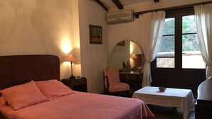 A bedroom with a bed, a nightstand, a lamp, a chair, a small table with a bowl, a mirror, and a window with curtains. - Secular Manor: Pool & 2.5ha Estate – Perfect for Families & Friends (Roussillon)