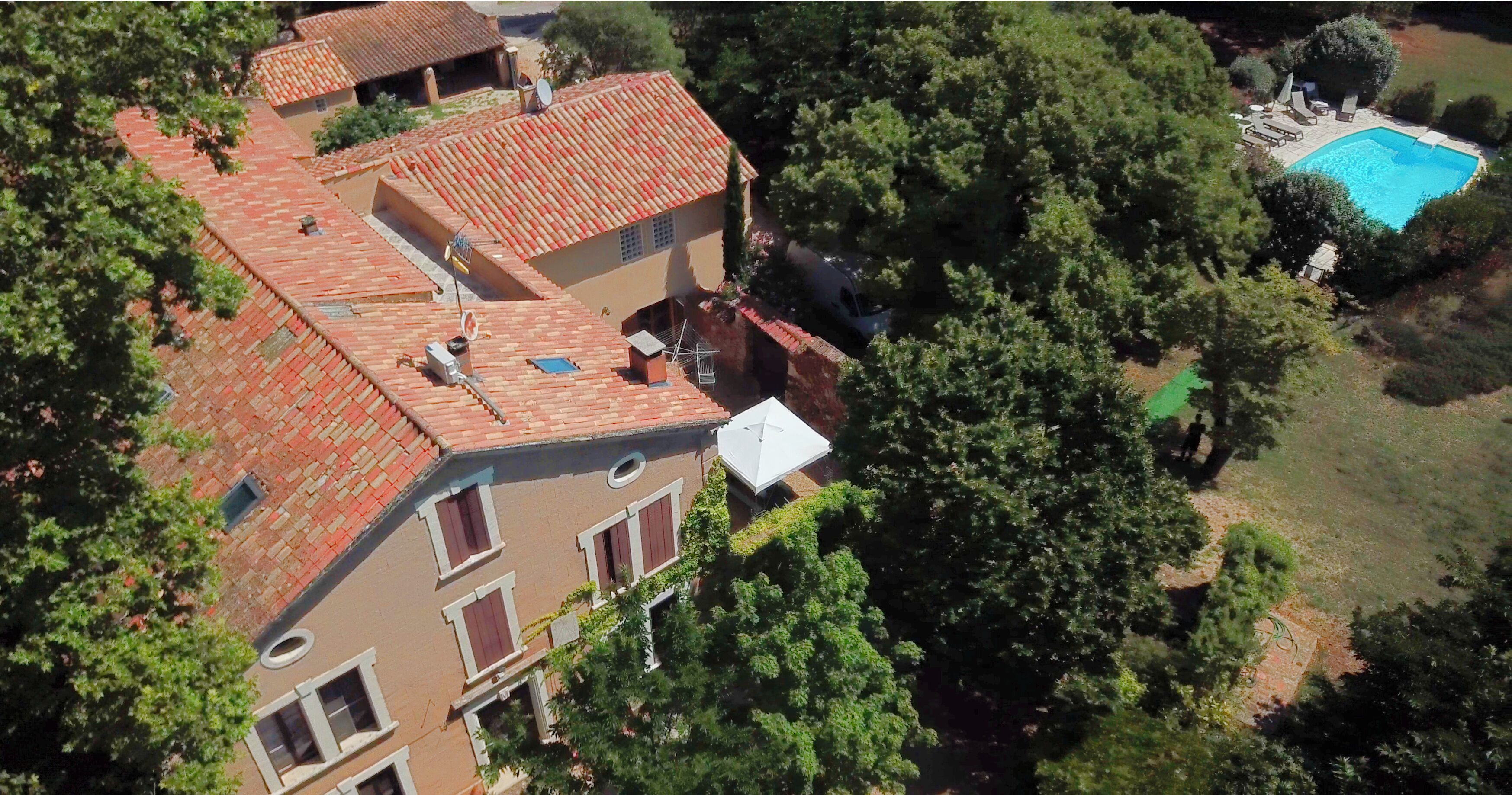 Un bâtiment à deux étages, doté d’un toit recouvert de tuiles rouges, d’une piscine et entouré de verdure.