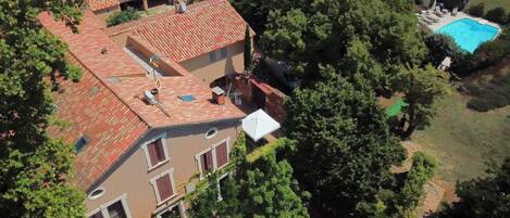 Un bâtiment à deux étages, doté d’un toit recouvert de tuiles rouges, d’une piscine et entouré de verdure.