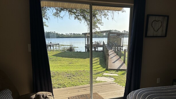 Une pièce dotée d’une grande porte-fenêtre coulissante donnant sur une terrasse extérieure avec un escalier en bois et une vue sur un lac.