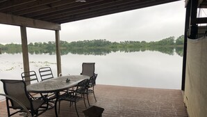 Un espace extérieur abrité, avec une table et des chaises, donnant sur un lac paisible, le tout entouré de verdure.