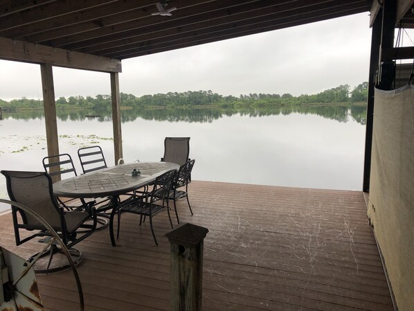Un espace extérieur abrité, avec une table et des chaises, donnant sur un lac paisible, le tout entouré de verdure.