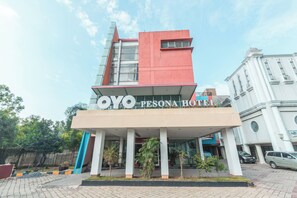 A hotel named 'OYO PESONA HOTEL' with a modern architectural design, featuring a prominent red and white facade, a covered entrance area, and a parking lot with cars. - Collection O Cikarang Near Pollux Mall Formerly Hotel Pesona Cikarang (Cikarang)