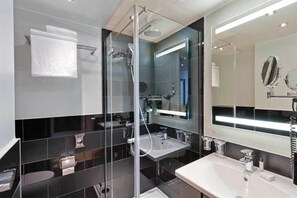 Ein modernes Badezimmer mit einer Duschkabine, einem großen Spiegel und einem weißen Waschbecken.