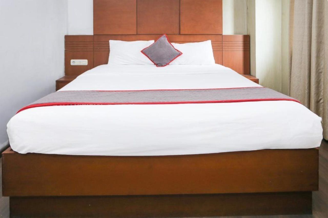 Un lit bien fait, avec une tête de lit en bois, une literie blanche et une bande décorative rouge.