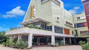 A modern building with a flat roof, large windows, and a covered entrance area with potted plants. - Collection O Cikarang Near Pollux Mall Formerly Hotel Pesona Cikarang (Cikarang)