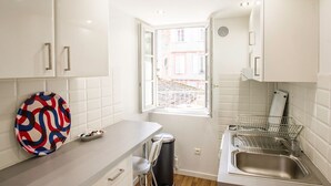 Une cuisine de taille réduite avec des meubles blancs, une fenêtre et un égouttoir à vaisselle.