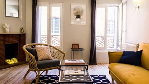 Un salon chaleureux avec un fauteuil en osier, un canapé, une table basse en verre et une cheminée.