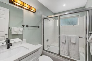 A modern bathroom with a glass-enclosed shower, a white sink, and a large mirror.