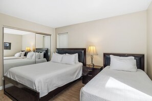 A hotel room with two beds, a large mirror, bedside lamps, and a window with blinds.