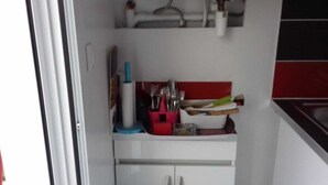 Una cocina con armarios blancos, salpicadero rojo y una encimera con utensilios y una tetera.