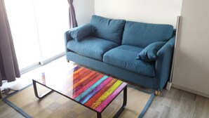 Una sala de estar con un sofá azul, una mesa de centro a rayas coloridas y una ventana con cortinas.