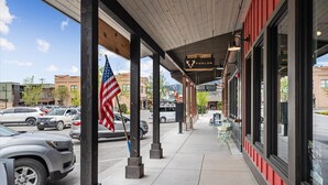 Un espacio exterior techado con fachada comercial, una bandera y automóviles estacionados.