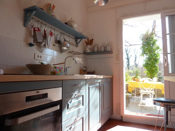 A kitchen with a built-in oven, a sink, and a window leading to an outdoor area with a yellow table and chairs.