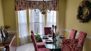 A dining room with a glass table, red patterned chairs, and a chandelier. - CrownCity Home Away From Home (Charlotte)