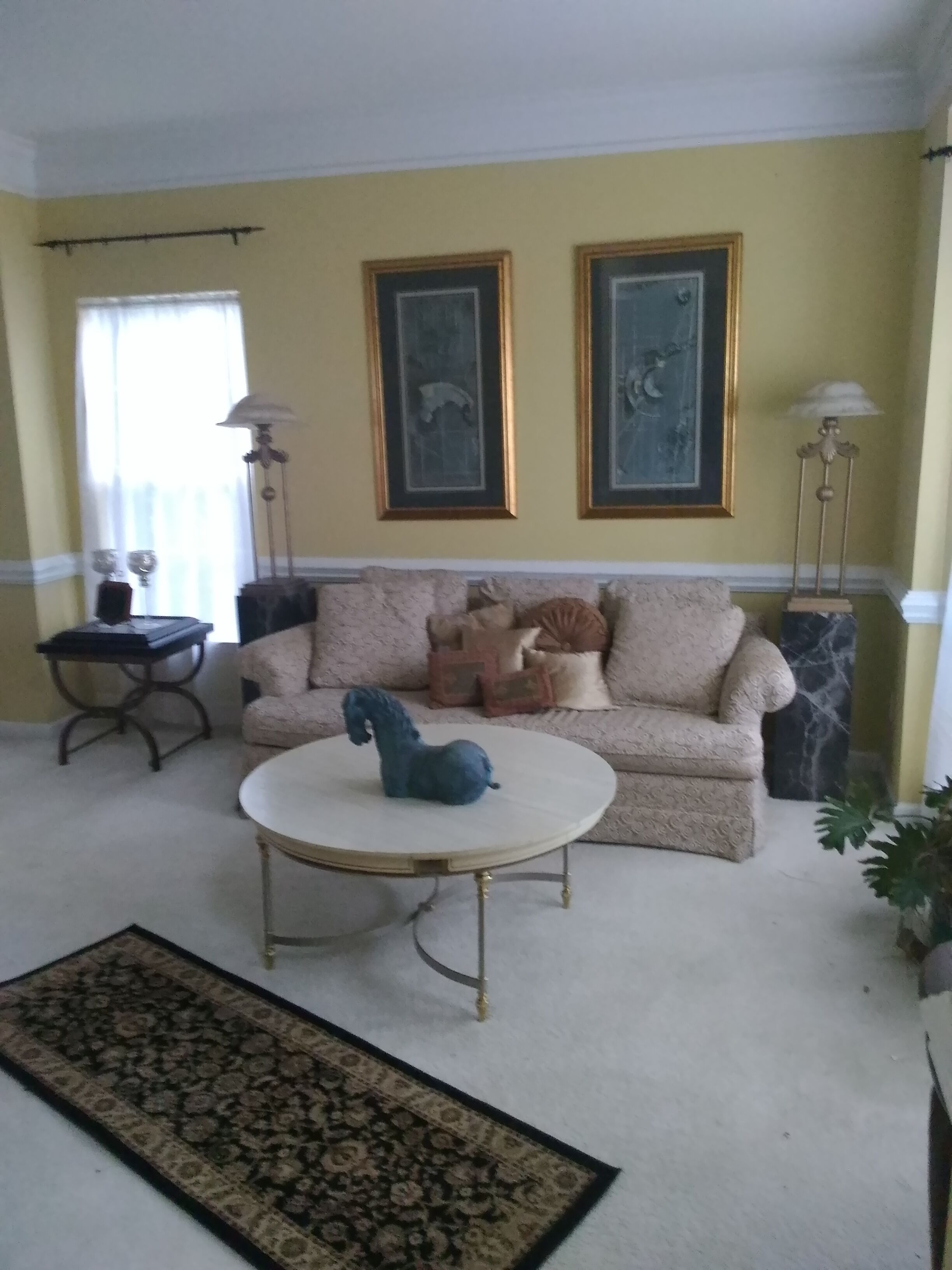 A living room with a beige sofa, a round coffee table, and two framed pictures on the wall.