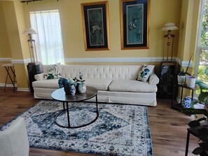 Un salon avec un canapé beige, un tapis à motifs et deux œuvres d’art encadrées accrochées au mur.