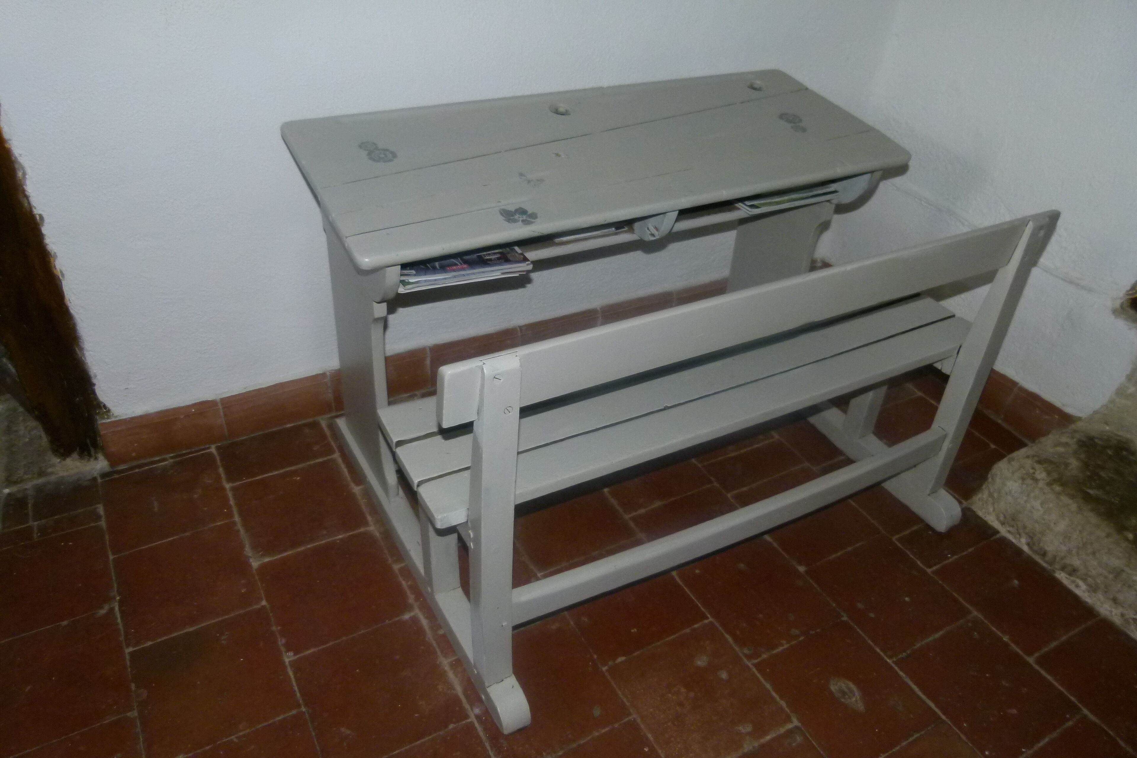 Une petite table en bois, blanche, avec un plateau plat et un banc fixé sur le côté.