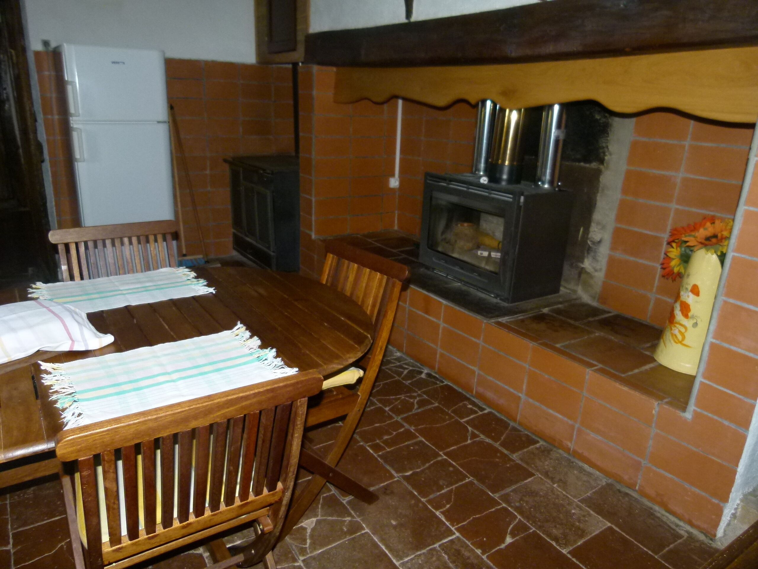 A kitchen with a tiled backsplash, a wood-burning stove, a refrigerator, and a dining table with chairs.