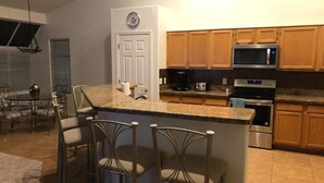 A kitchen with a central island, bar stools, wooden cabinets, a microwave, a toaster, a coffee maker, and a clock on the wall. - Very nice 4 bdrm 2 full bath ranch home w/ great room in quiet neighborhood. (Phoenix)