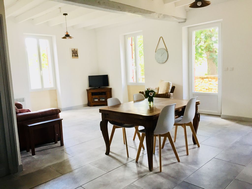 Een ruime eethoek met een houten tafel en stoelen, een televisie en een raam met uitzicht op groen.