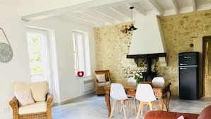 A cozy living room with a wicker sofa, a brown leather couch, a dining table with white chairs, a stone wall, and a black refrigerator. - Beautifully restored 2 bedroom house with private pool and barbecue. (Thénac)