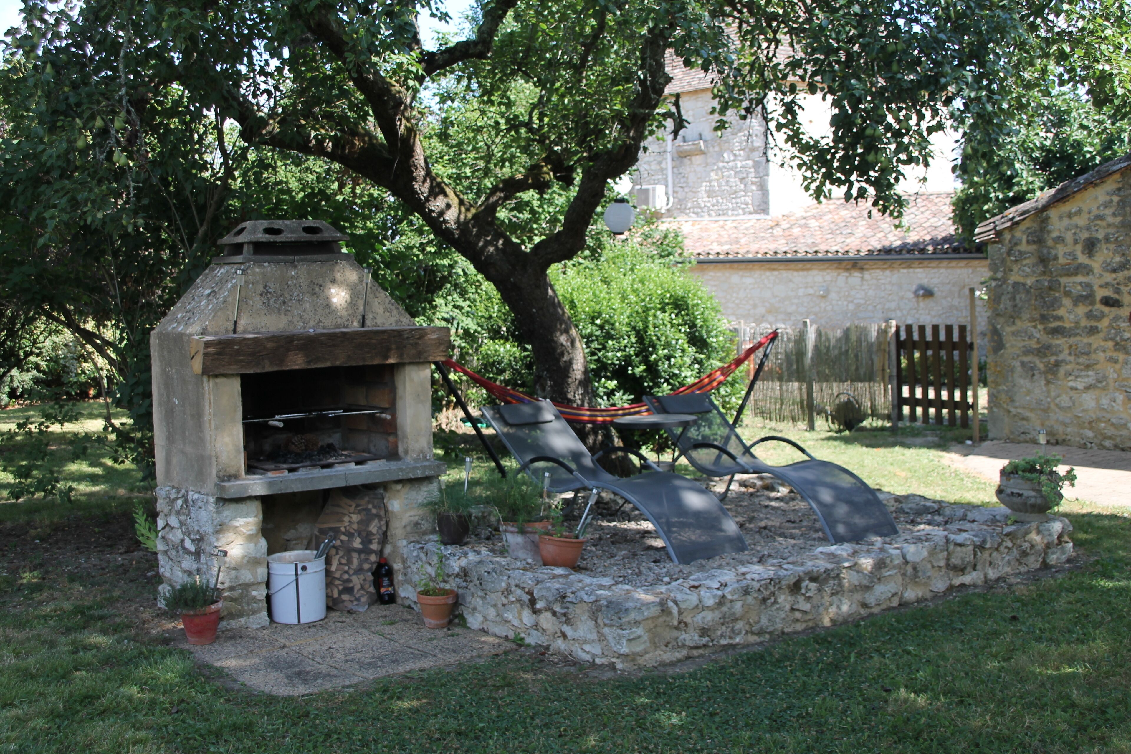 An outdoor kitchen area with a stone oven, surrounded by potted plants and a hammock.