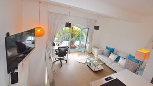 A modern living room with a flat-screen TV, a sofa, a coffee table, and a dining area with a chair and table. - LOVELY DUPLEX IN A PALACE (Beausoleil)