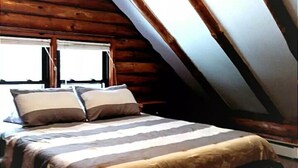 A bedroom with a sloped ceiling, wooden beams, a bed with striped bedding, and two windows. - Private Brook Side Log Cabin  on Tenney Mountain (Plymouth)
