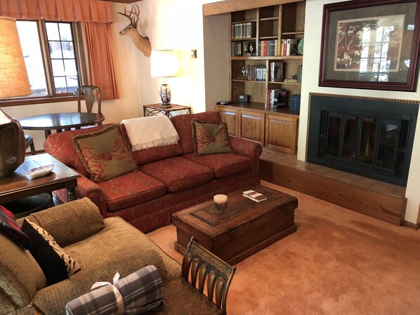 A cozy living room with a red sofa, a wooden coffee table, and a fireplace.