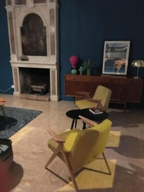 A room with a fireplace, a yellow armchair, a black armchair, a wooden cabinet, and a framed picture on the wall.
