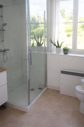 Ein modernes Badezimmer mit Duschkabine aus Glas, Toilette und einem Fenster mit Pflanzen.