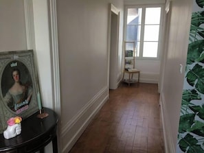 Un pasillo con suelo de madera, un cuadro enmarcado sobre una mesa y una ventana con vistas al exterior.