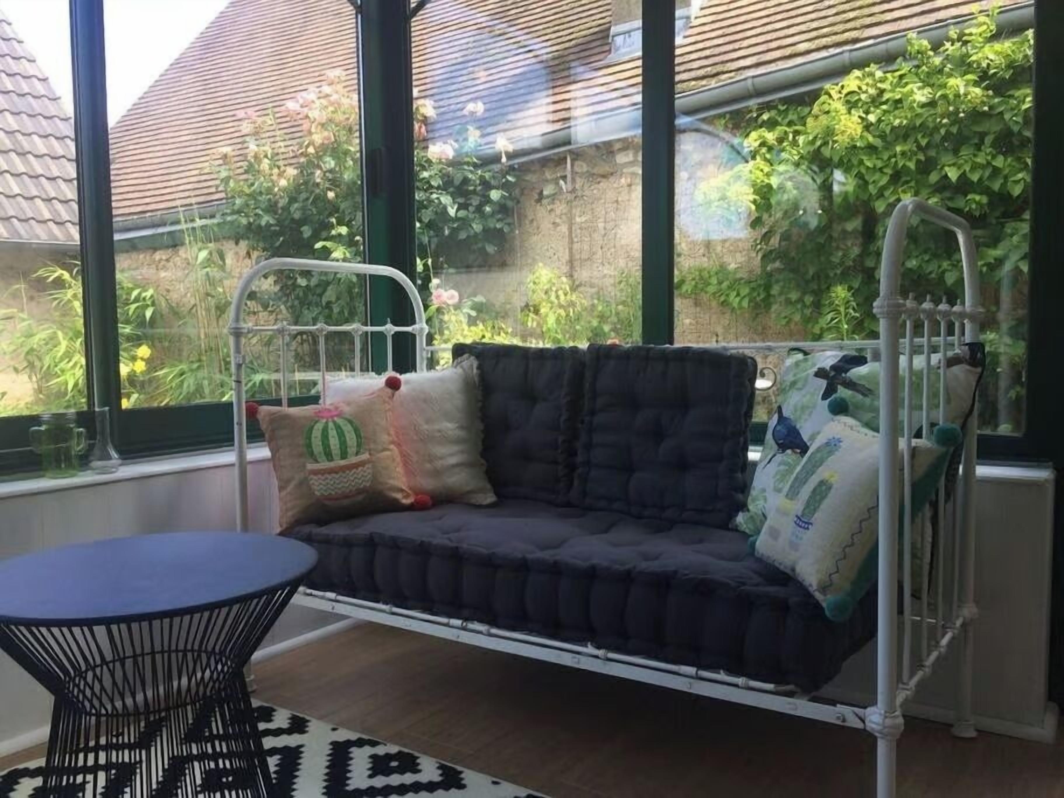 A room with a metal swing bed, a round table, and a view of a garden through large windows.