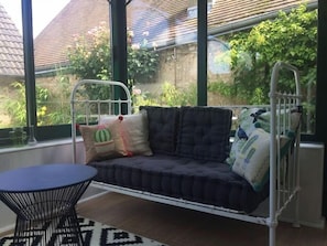 Una habitación con una hamaca metálica, una mesa redonda y vistas a un jardín a través de amplios ventanales.