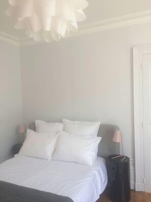 A bedroom with a bed, pillows, a bedside lamp, and a suitcase.